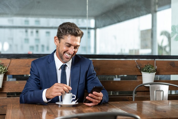 Vrolijke mannelijke executive browsen mobiele telefoon in cafetaria