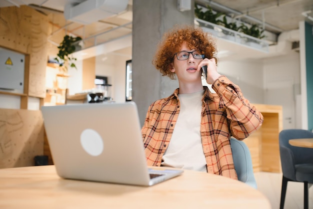 Vrolijke mannelijke freelancer die telefoongesprek voert, deelt goed nieuws over project dat in café-interieur werkt