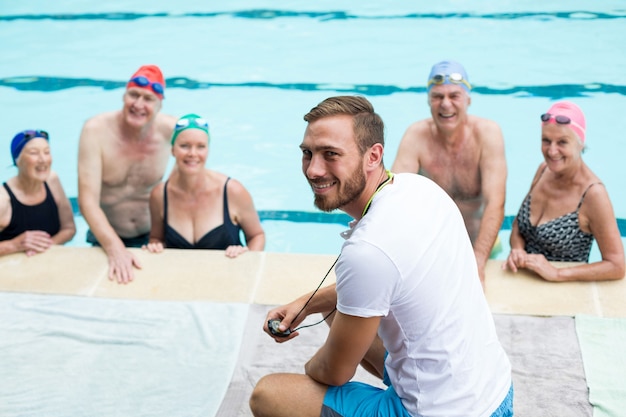 Vrolijke mannelijke instructeur senior zwemmers bijstaan bij het zwembad