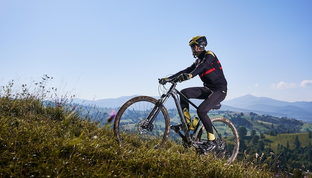 Vrolijke mannelijke wielrenner fiets bergop onder de blauwe hemel