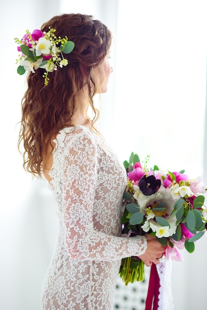 Vrolijke meisjesbruid in een witte gebreide jurk poseren met een boeket bloemen