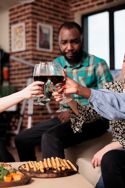 Vrolijke mensen die wijnglazen roosteren terwijl ze thuis verjaardag vieren. Diverse groep goede vrienden op wijnfeest rammelende glazen terwijl ze samen genieten van leuke tijd in de woonkamer.