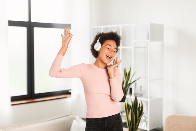 Vrolijke millennial afro-amerikaanse vrouw in draadloze koptelefoon zingt lied geniet van favoriete muziek dansen