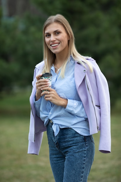 Vrolijke modieuze blonde koffie buiten te houden. Jonge vrouw koffie drinken op straat van de stad.