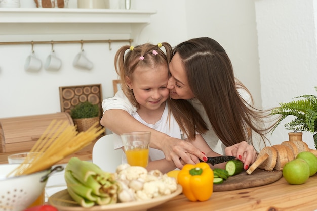 Vrolijke moeder en dochtertje bereiden samen salade in de keuken en hebben plezier. Het meisje kust haar moeder thuis.