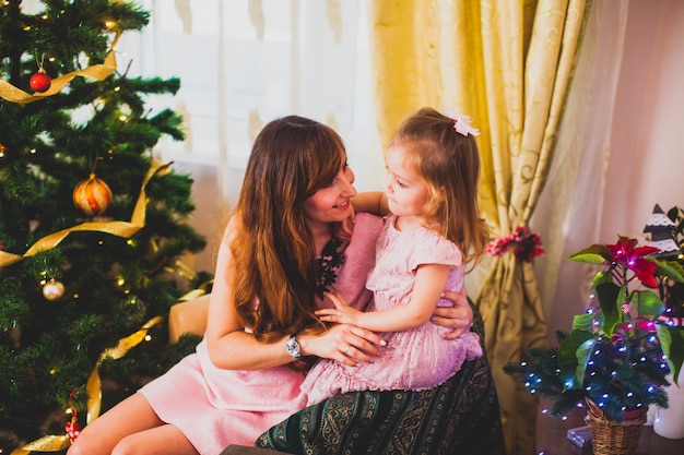 Vrolijke moeder en haar schattige dochtermeisje hebben plezier in de buurt van de kerstboom thuis Liefdevolle familie vieren nieuwjaar