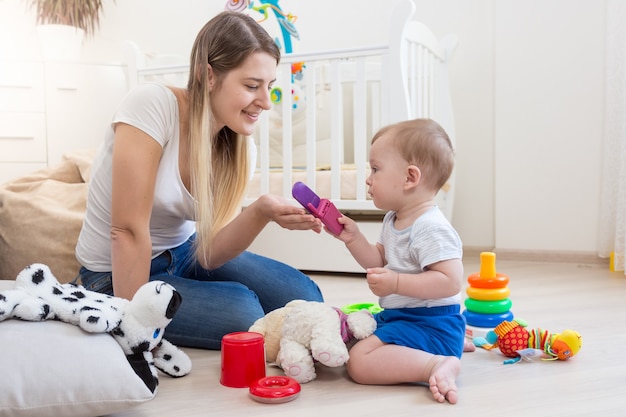 Vrolijke moeder en haar zoontje op de vloer spelen met speelgoed