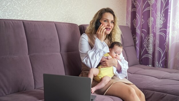 Foto vrolijke moeder praat op smartphone met babymeisje in armen