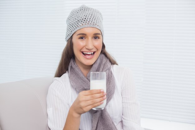 Vrolijke mooie brunette met de winterhoed op het houden van glas melk