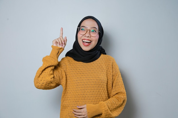Vrolijke mooie jonge Aziatische moslim zakenvrouw met oranje trui en bril denkend