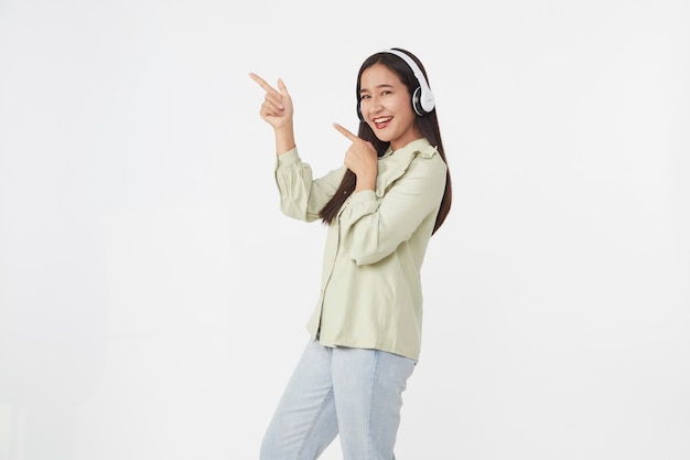 Vrolijke mooie jonge Aziatische vrouw dansen genieten van muziek in draadloze koptelefoon op wit oppervlak