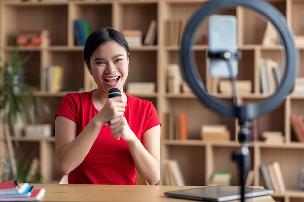 Vrolijke mooie jonge Japanse vrouwelijke superster die zingt op microfoonschietblog op smartphone