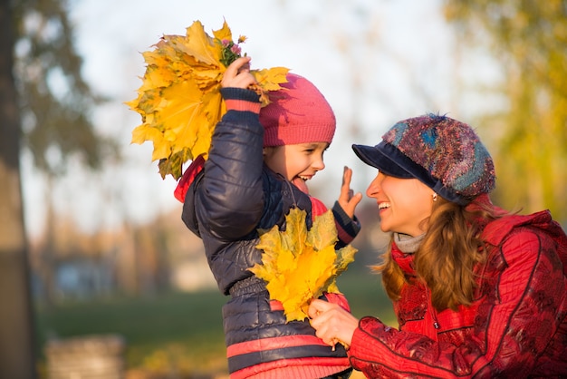 Vrolijke mooie moeder met haar dochter herfstbladeren te houden