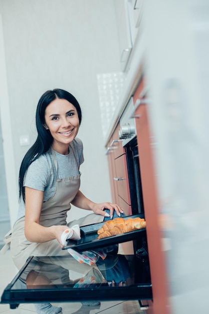 Vrolijke mooie vrouw in de keuken met een hete bakpan met heerlijke croissants