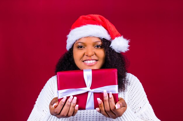 Vrolijke mooie vrouw in rode kerstman hoed lachen geïsoleerd op rode achtergrond ze is blij en opgewonden vol plezier met geschenkdoos
