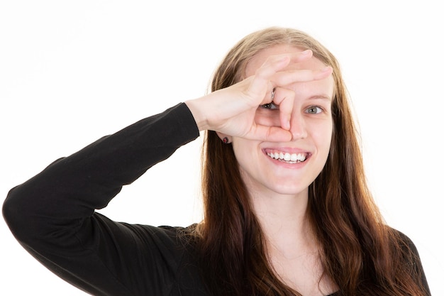 Vrolijke mooie vrouw met open mond vingers hand op oog aanbrengen en Ok gebaar maken op witte achtergrond