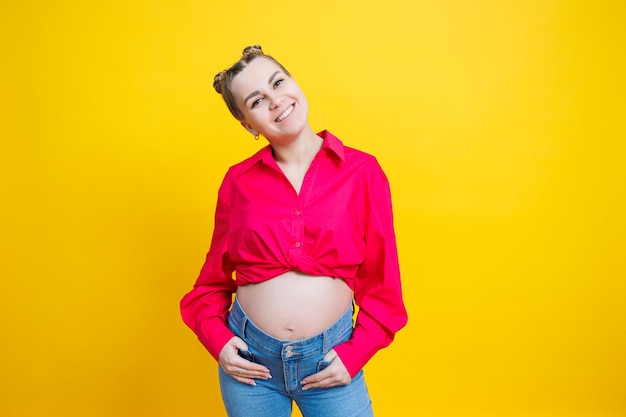 Vrolijke mooie zwangere vrouw in een roze shirt op een gele achtergrond Jonge lichte zwangere vrouw