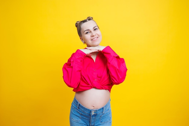 Vrolijke mooie zwangere vrouw in een roze shirt op een gele achtergrond Jonge lichte zwangere vrouw