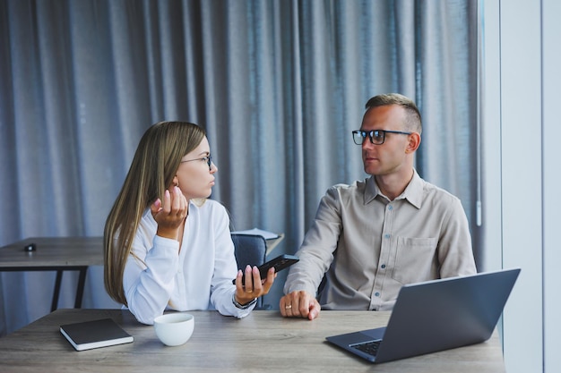 Vrolijke ondernemers die een laptop gebruiken in een kantoor Gelukkige jonge ondernemers die glimlachen terwijl ze samenwerken in een moderne werkruimte Twee jonge ondernemers die samen aan een tafel zitten