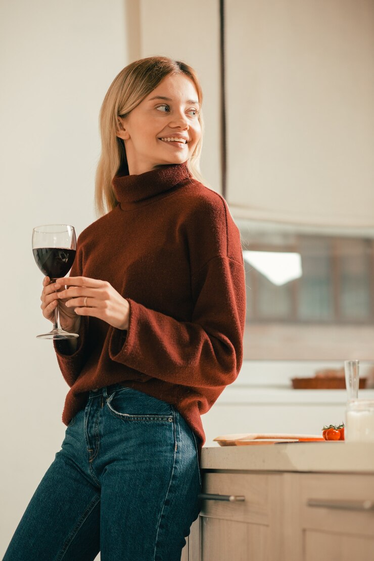 Vrolijke ontspannen dame die alleen staat met een glas wijn en glimlacht terwijl ze in de verte kijkt