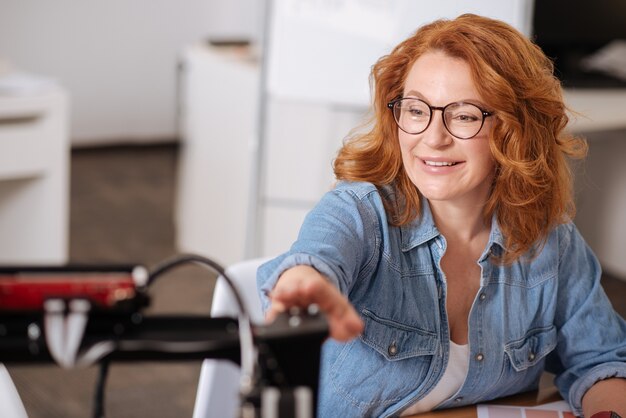 Vrolijke opgetogen aardige vrouw die naar de 3d-printer kijkt en lacht terwijl ze ermee werkt