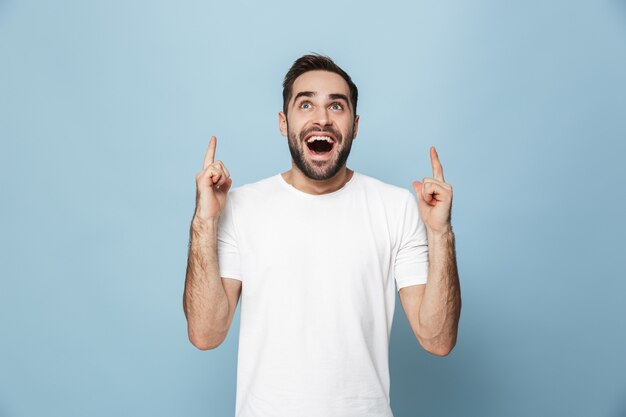 Vrolijke opgewonden man met een leeg t-shirt dat geïsoleerd over een blauwe muur staat en kopieerruimte presenteert