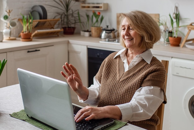 Vrolijke oudere vrouw die informatie controleert op een laptop online videogesprek met kinderen of vrienden die bezig zijn