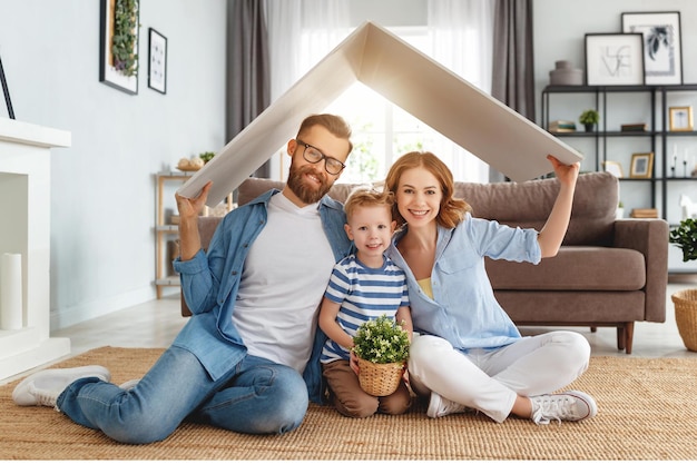 Vrolijke ouders met kinderen die glimlachen en dakmodel boven het hoofd houden terwijl ze op de vloer zitten in een gezellige woonkamer tijdens verhuizing