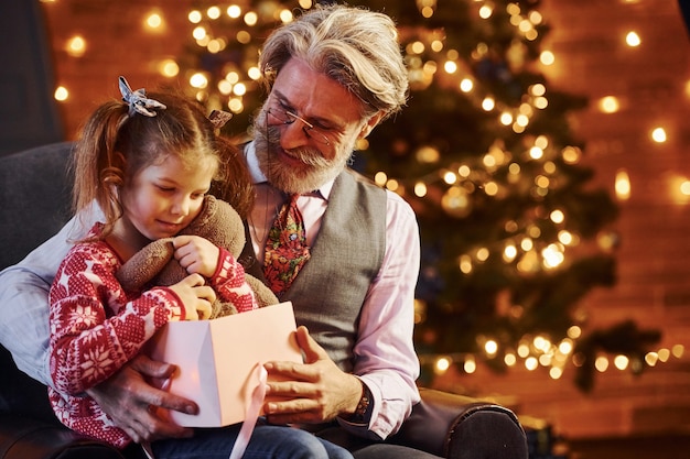 Vrolijke ouderwetse senior man met grijs haar en baard met meisje met geschenkdoos.