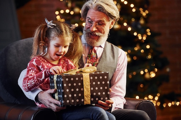 Vrolijke ouderwetse senior man met grijs haar en baard met meisje met geschenkdoos.