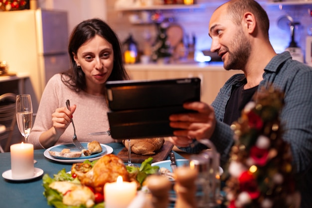 Vrolijke paar eten heerlijk diner zittend aan tafel in kerst ingerichte keuken