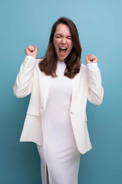 Vrolijke positieve brunette vrouw in witte jurk die zich voordeed als model op studio achtergrond