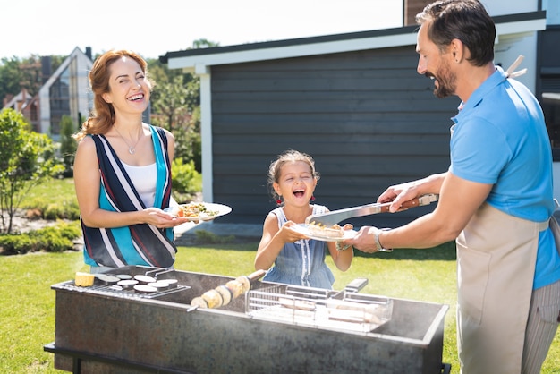 Vrolijke positieve man die eten serveert terwijl hij een picknick heeft met zijn gezin