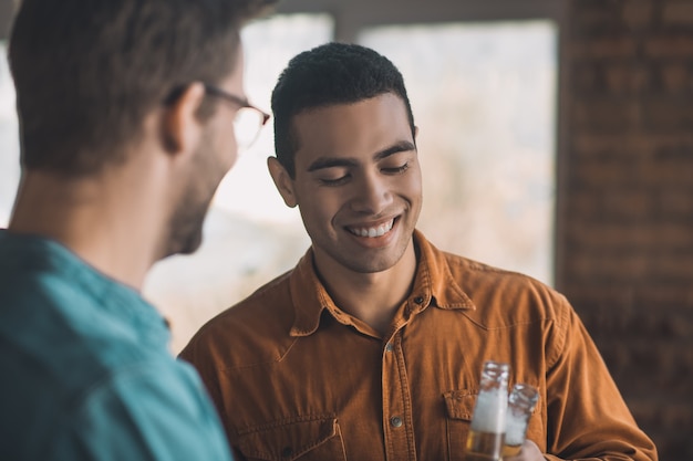 Vrolijke positieve man die lacht terwijl hij bier drinkt met zijn vriend