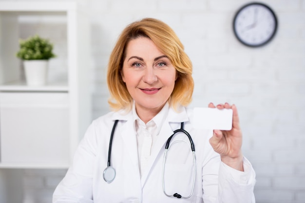 Foto vrolijke rijpe vrouwelijke arts die haar visitekaartje toont