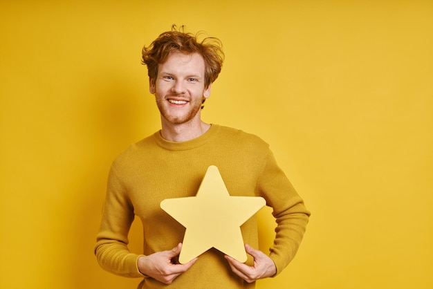 Vrolijke roodharige man met een stervormige banner terwijl hij tegen een gele achtergrond staat