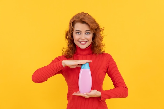 Vrolijke roodharige vrouw met krullend geverfd haar met lichaamsverzorgingsproduct van shampoo-reclame