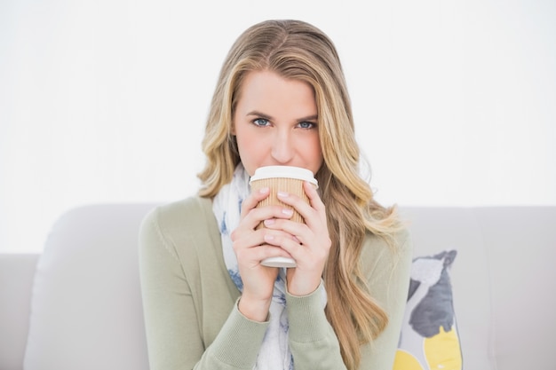 Vrolijke schattige blonde drinken koffie zittend op een gezellige sofa