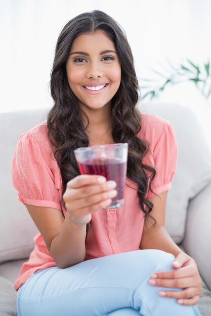 Vrolijke schattige brunette zittend op de bank holding glas sap