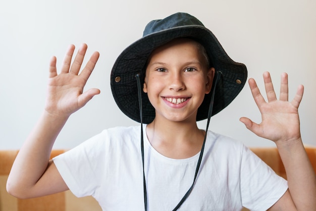 Vrolijke schoolgaande jongen die lacht terwijl hij naar de camera kijkt in een wit t-shirt en een zwarte zonnehoed kan...