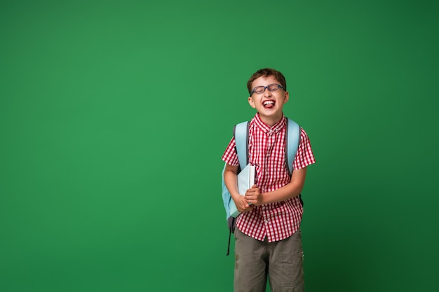 Vrolijke schooljongen die met glazen boek en rugzak houdt