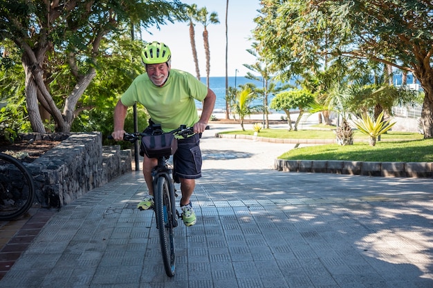 Vrolijke senior actieve man rijden op zee met zijn elektrische fiets en gele helm - horizon over zee, gezonde levensstijl voor oudere gepensioneerden, concept van vakantie en sport