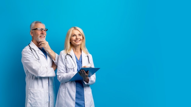 Vrolijke senior artsen kijken naar kopie ruimte blauwe achtergrond