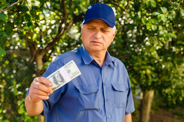 Vrolijke senior holdingsgeldbundels op de tuinachtergrond