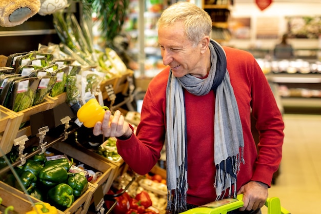 Vrolijke senior man die groenten kiest bij supermarkt