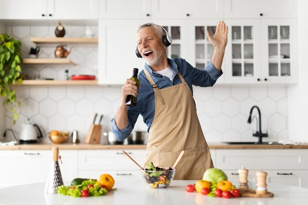 Vrolijke senior man die plezier heeft tijdens het koken in de keuken zingen en dansen