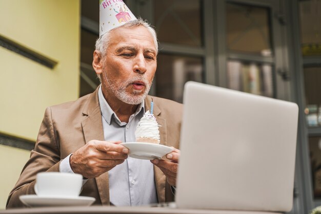 Vrolijke senior man viert verjaardag met videocall op café terras