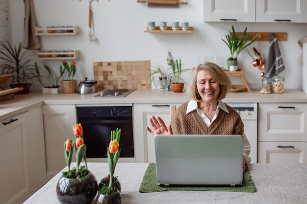 Vrolijke senior vrouw die informatie controleert over laptop online videogesprek met kinderen