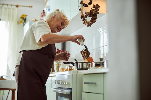 Vrolijke senior vrouw in schort koken diner in de keuken