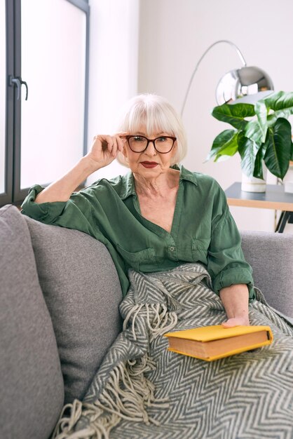 vrolijke senior vrouw zittend op de bank thuis een boek te lezen